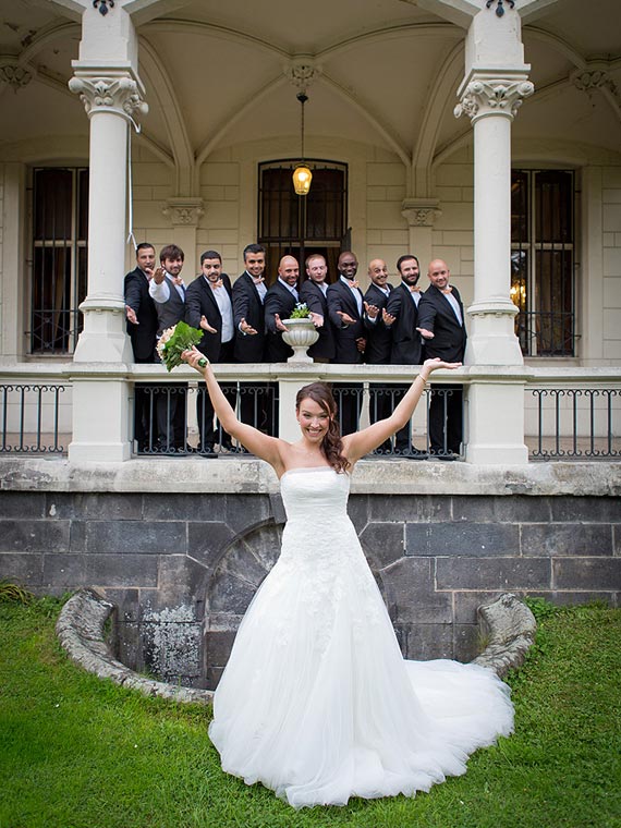 Bride throwing arms in the air, with groom & groomsmen