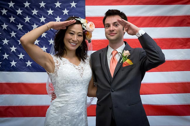 Bride and groom saluting before the Stars and Stripes